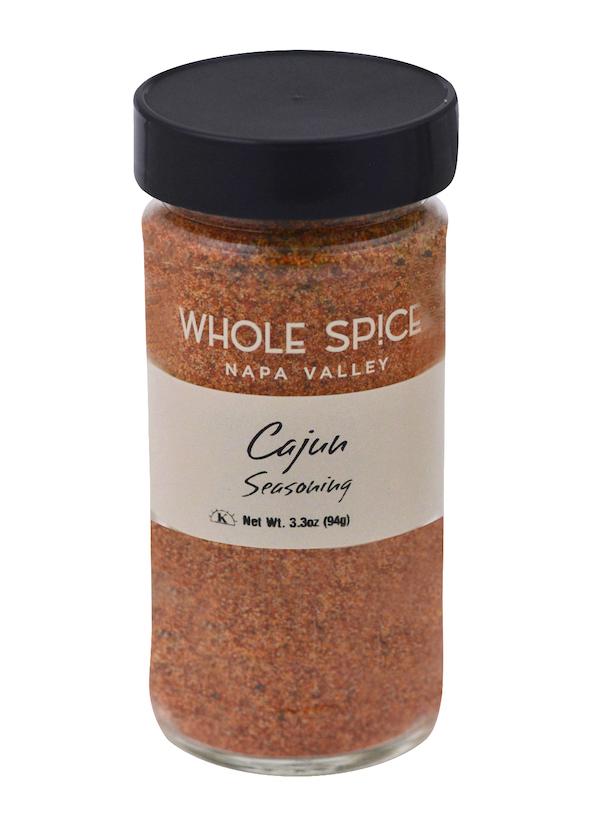 A clear glass jar with a black lid, labeled Whole Spice Inc. Cajun Seasoning, holds a reddish-brown blend. Net weight: 3.3 oz (94g).