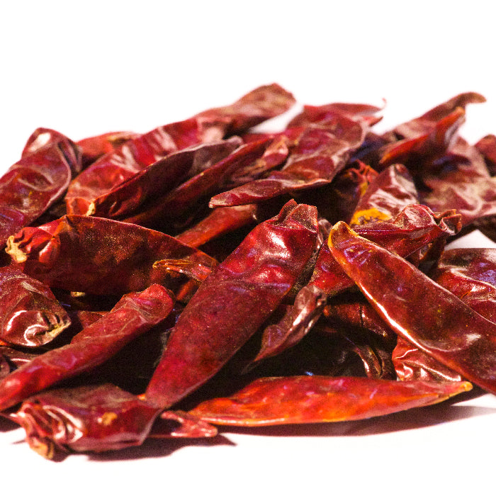 A pile of Whole Spice Inc. Calabrian Chili Whole peppers is shown on a white background. The glossy, wrinkled chilies are fully dried and perfect for adding authentic Italian flavor or making homemade pepper flakes.