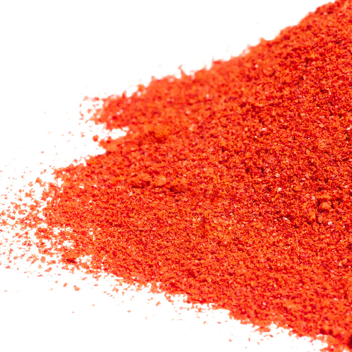 A close-up of bright red, finely ground California Chili Powder by Whole Spice Inc., scattered on a white surface.