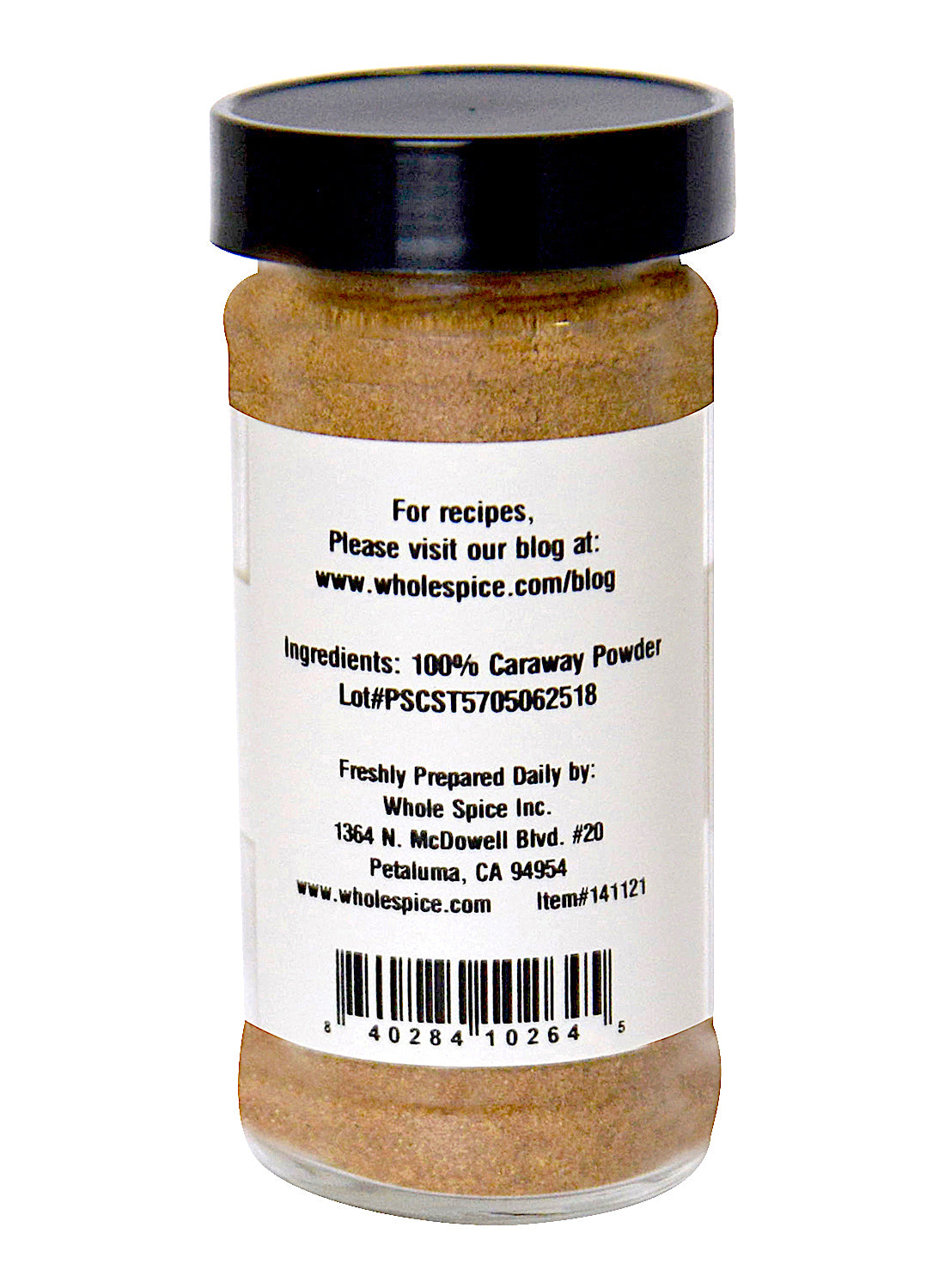 A clear spice jar with a black lid contains 100% Caraway Seed Powder by Whole Spice Inc. The label shows ingredients, company info, barcode, and recipe website. Address: Petaluma, California.