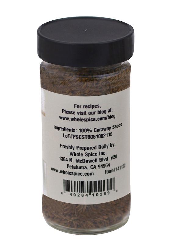 A glass spice jar from Whole Spice Inc. with a black lid contains brown Caraway Seeds (100% caraway seeds). The label includes company contact info, a website for recipes, and notes it's ideal for flavoring rye bread.