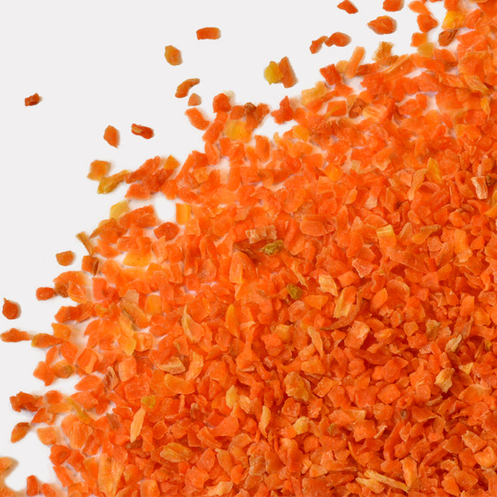 A close-up of Whole Spice Inc. Carrot Large ¼” Granules, rich in vitamin A, scattered across a white surface and dominating the image.