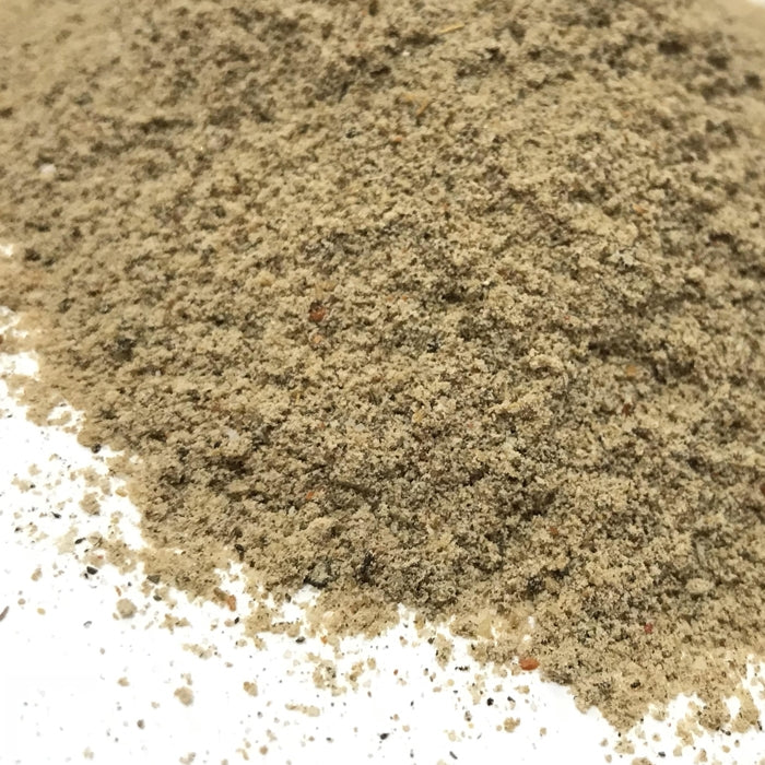 A close-up of finely ground, light brown and speckled Chaat Masala by Whole Spice Inc. is spread on a white surface, capturing the essence of this classic Indian spice blend used in South Asian cuisine.