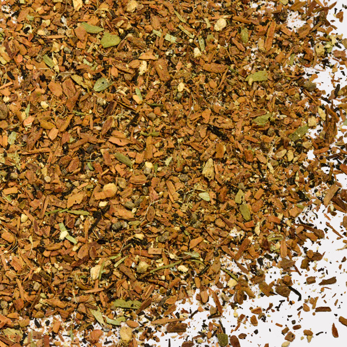 A close-up of Whole Spice Inc.'s Chai shows a mix of dried herbs and spices with brown and green flecks scattered on a white background.