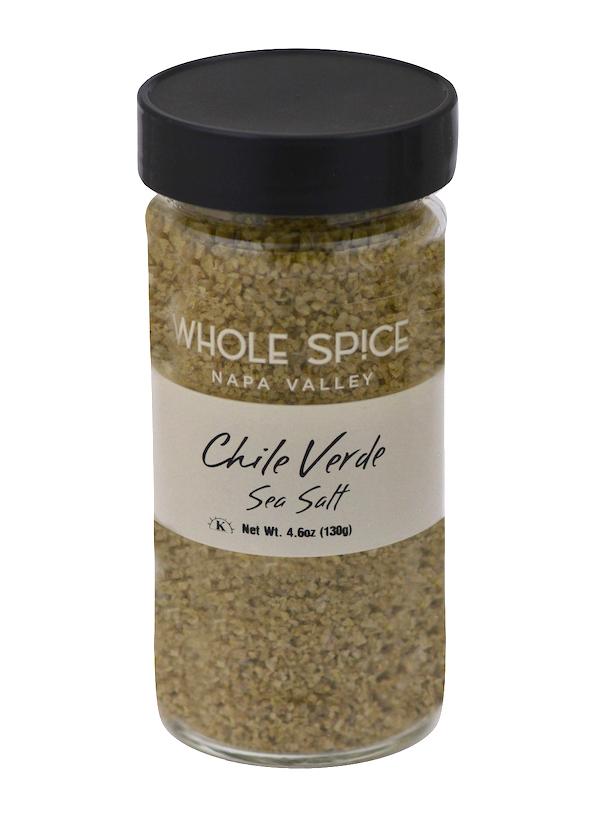 A clear glass jar with black lid, labeled Whole Spice Inc. Chili Verde Sea Salt, contains coarse greenish spicy salt blended with green chili powder. Net weight: 4.6 oz (130g).