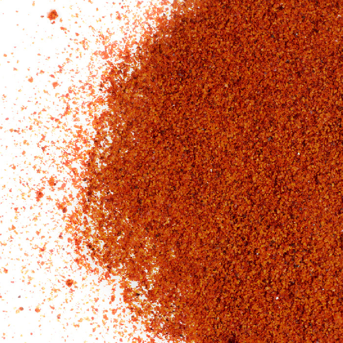 A close-up of bright red Chili BBQ Spice Rub by Whole Spice Inc., scattered on a white surface—ideal as a spicy blend for your favorite grill seasoning.