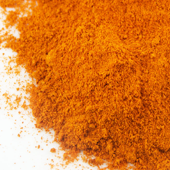 A close-up of Whole Spice Inc. Cayenne Chili Powder Organic, a vibrant orange chili spice, spread out on a white surface.