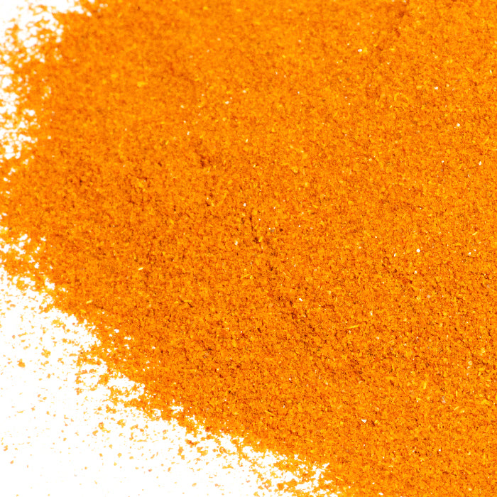 A close-up of Chili De Arbol Powder from Whole Spice Inc.—a vibrant, bright orange-red Mexican chili pepper powder—spread across a white surface.