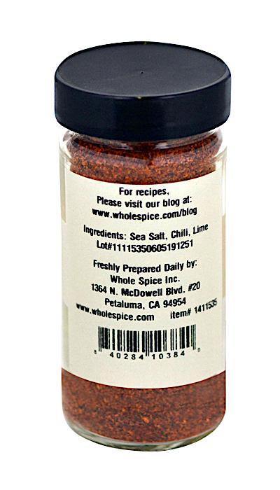 A clear spice jar with a black lid contains Whole Spice Inc.’s Chili Lime Salt, featuring sea salt, chili, and lime; ideal for seasoning fruit or rimming margaritas. The label includes the website, address, and product details.