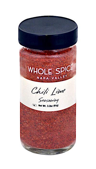 A glass jar of Whole Spice Inc. Chili Lime Seasoning with a black lid contains red, spicy fruit seasoning. The front label shows the product name and net weight: 3.2 oz (91g).