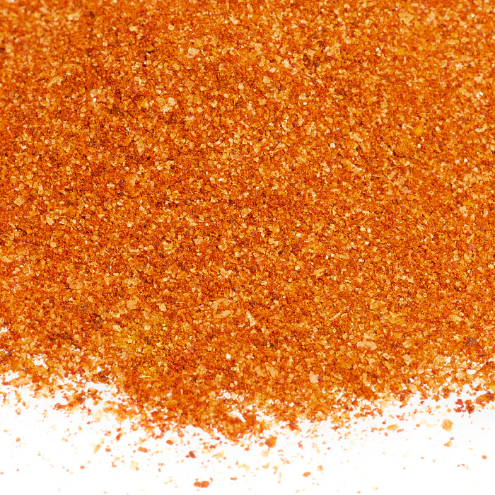 A close-up of Whole Spice Inc. Chili Lime Seasoning, a vibrant orange-red blend finely ground and spread on a white surface, captures its zesty flavor.