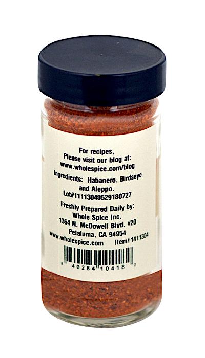 A clear glass spice jar with a black lid, filled with reddish-orange powder. The label reads "Chili Spice Blend - Fiery Hot" by Whole Spice Inc., highlighting Habanero, Birdseye, and Aleppo Chile Peppers plus contact details.