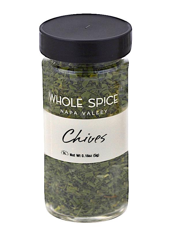 A clear spice jar with a black lid contains finely chopped green chives from Whole Spice Inc., labeled "Chives" and weighing 0.16oz (5g). The dried herb from the onion family is visible inside.