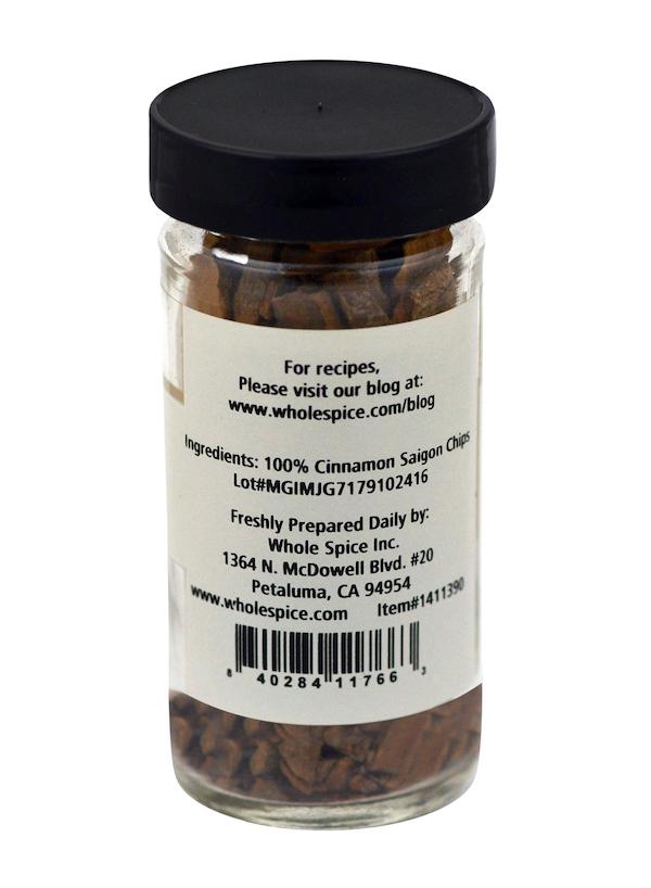 A glass jar with a black lid holds aromatic Cinnamon Chips Saigon by Whole Spice Inc. The label states “100% Cinnamon Saigon Chips” and features an address and website for recipes, emphasizing high-quality Indonesian cinnamon.