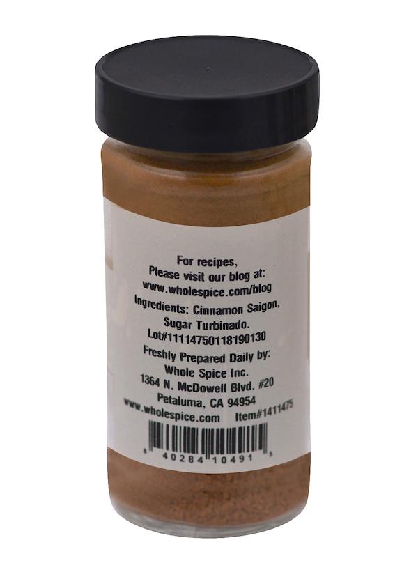 A spice jar labeled "Cinnamon Sugar" by Whole Spice Inc. lists Saigon cinnamon and demerara sugar as ingredients. The white label also has a website, address, barcode, and lot number. The jar contains brown powder ideal for cinnamon toast.