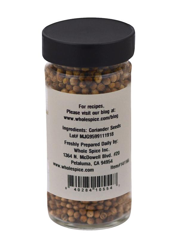 A clear spice jar from Whole Spice Inc. labeled "Coriander Seeds" comes with a black lid, ingredient and contact info, recipe blog link, and a barcode—perfect for pickling spices or Thai curries.