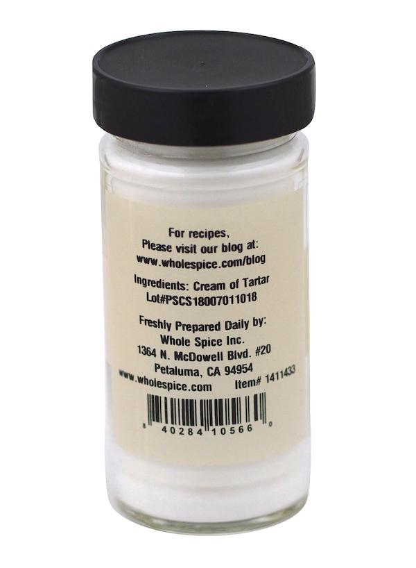 A clear spice jar with a black lid holds Whole Spice Inc. Cream of Tartar, a versatile baking ingredient for stabilizing egg whites. The back label lists ingredients, brand contact info, and features a barcode at the bottom.