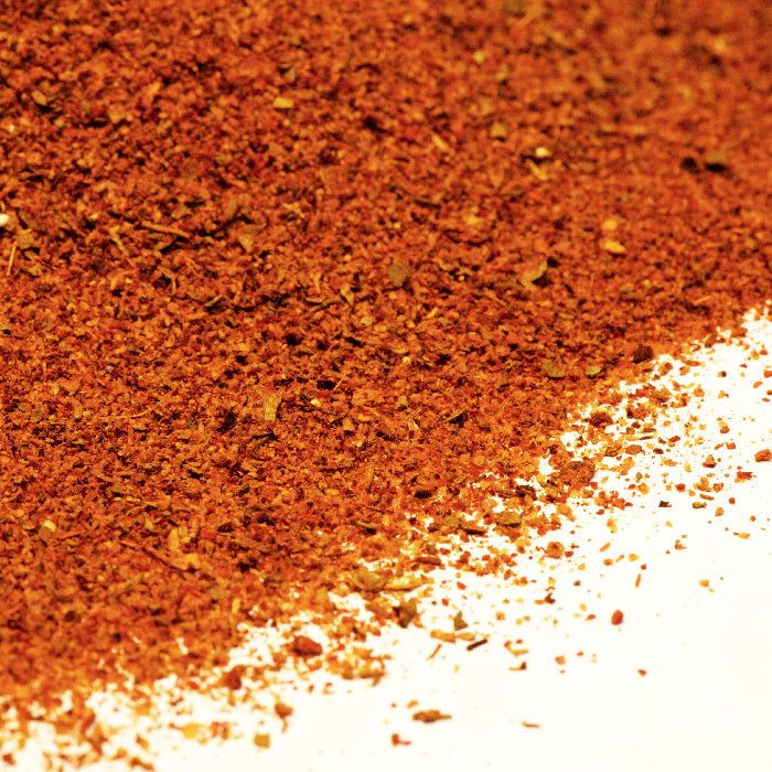 A close-up of Whole Spice Inc. Creole Seasoning, a finely ground reddish-brown blend scattered on a white surface—an ideal New Orleans seasoning base for various dishes.