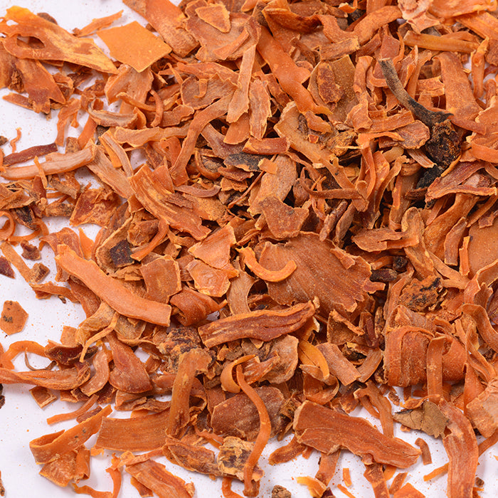 Close-up of Mace Whole by Whole Spice Inc., fragrant orange-brown shavings related to nutmeg, often used in French cuisine, scattered on a white surface.
