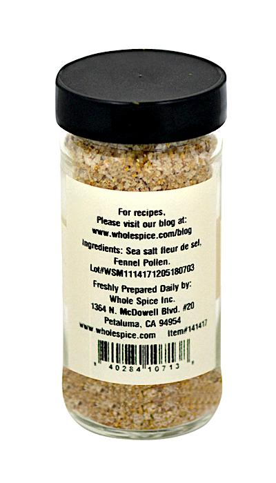 A clear glass jar with a black lid holds Whole Spice Inc. Fennel Salt, a coarse beige seasoning of sea salt and fennel pollen. The label includes ingredients, a website, address, and barcode.