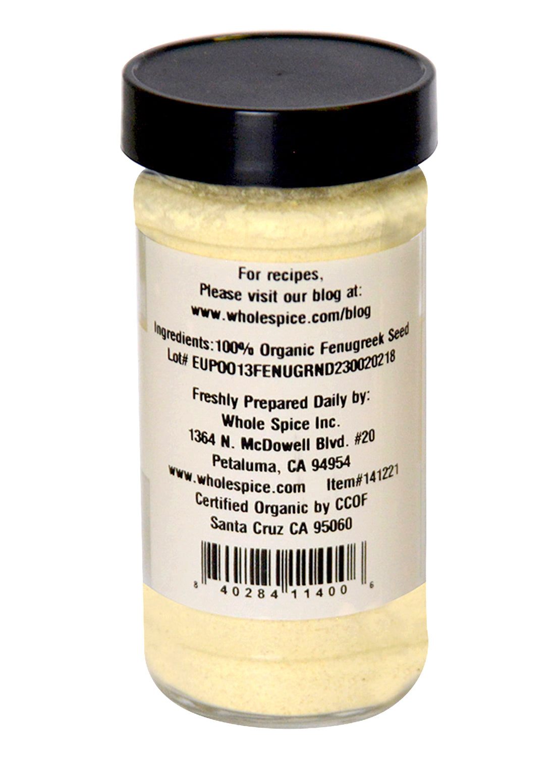 A clear spice jar with a black lid from Whole Spice Inc. contains Fenugreek Powder Organic, made from 100% fenugreek seeds. The label includes manufacturer info and a website for recipes. The powder inside is pale yellow.