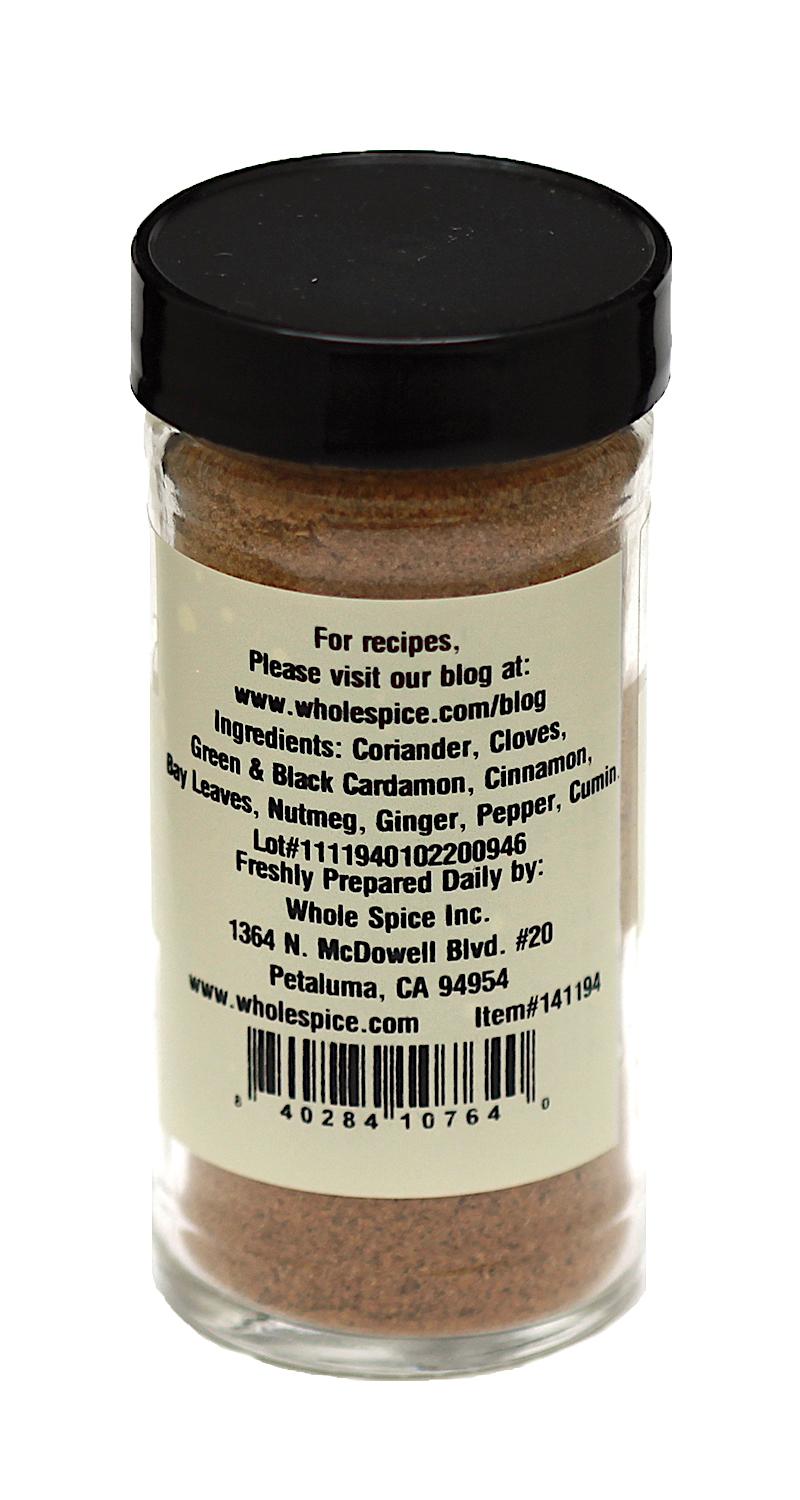 A clear Garam Masala spice jar from Whole Spice Inc. with a black lid features a label listing classic spices—coriander, cloves, cardamom, cinnamon, nutmeg, ginger, pepper, cumin—plus company info and website for recipes.
