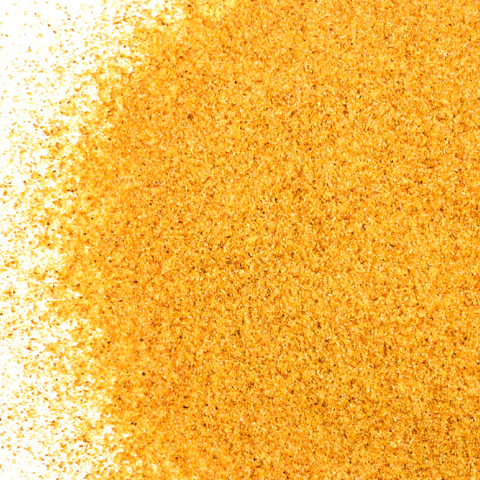 A close-up of Whole Spice Inc. Garlic Roasted Granulated, golden-yellow grains scattered on a white background, forming a textured surface that fades left—ideal for adding Mediterranean flavor to your dishes.
