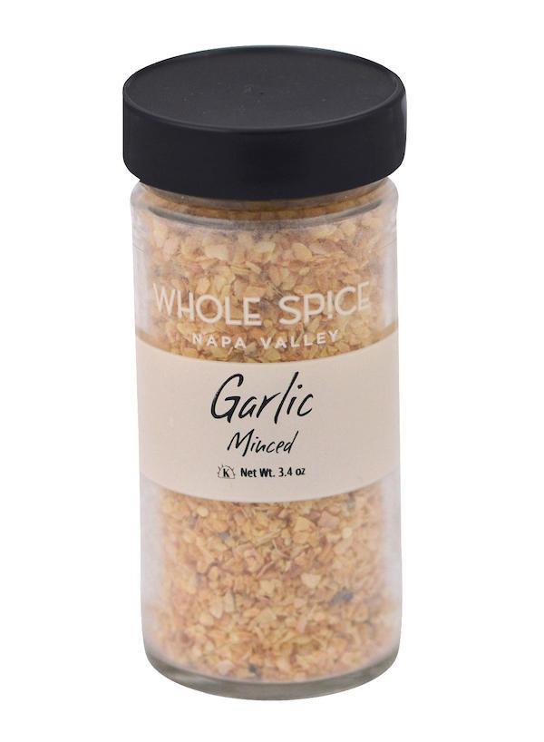 A clear glass jar with a black lid holds Whole Spice Inc. Garlic Minced. The beige label reads "Garlic Minced," showcasing this convenient dehydrated garlic seasoning with a net weight of 3.4 oz.