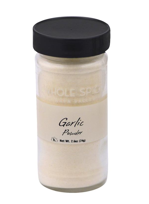A clear glass jar with a black lid holds Whole Spice Inc. Garlic Powder, Net Wt. 2.6 oz (74g)—perfect for seasoning your dishes with bold garlic flavor.