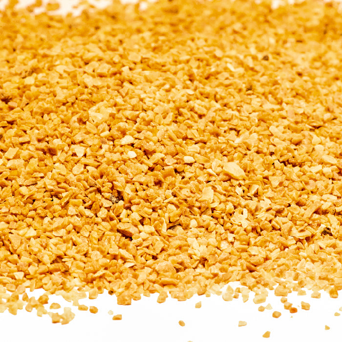 A close-up view of a pile of Whole Spice Inc. Garlic Minced Organic, showcasing small, golden-yellow granules spread across a white surface.