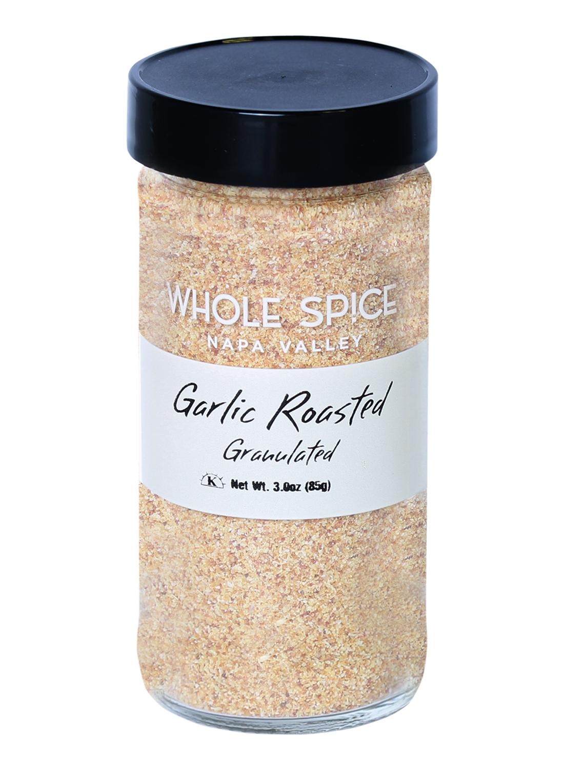 A clear glass jar with a black lid holds Whole Spice Inc. Garlic Roasted Granulated, ideal for Mediterranean dishes. The label says: Whole Spice Inc. Garlic Roasted Granulated Net Wt. 3 oz (85g).