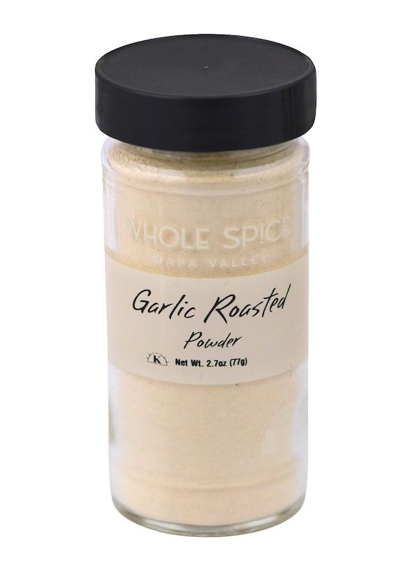 A clear glass jar with a black lid holds light beige Garlic Roasted Powder by Whole Spice Inc., ideal for Mediterranean dishes. The label states “Garlic Roasted Powder, Whole Spice Inc., Net Wt. 2.7oz (77g).”.