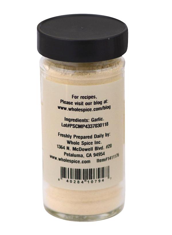 A clear glass jar with a black lid contains Garlic Roasted Powder from Whole Spice Inc. The label lists garlic as the sole ingredient and includes supplier contact details, making it ideal for Mediterranean dishes.