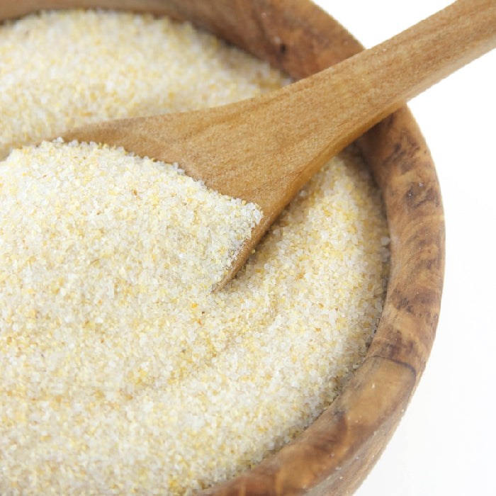 A wooden bowl with coarse yellow and white cornmeal and a wooden spoon, ready to be mixed with Whole Spice Inc. Garlic Salt for added flavor.