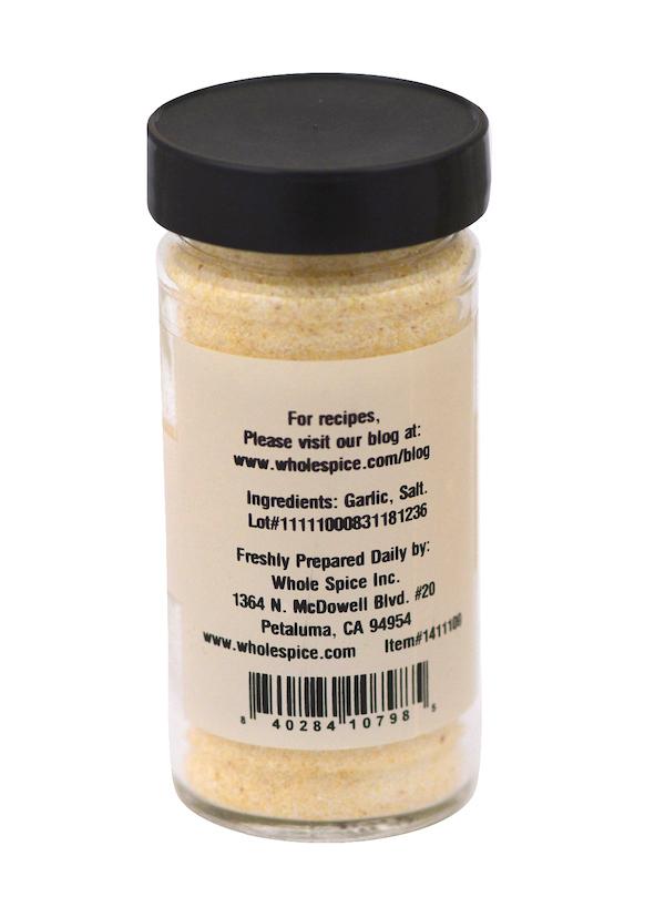 A clear spice jar labeled "Garlic Salt" by Whole Spice Inc. features a black lid, lists garlic and sea salt as ingredients, and includes company info, condiment details, and a barcode on the back.