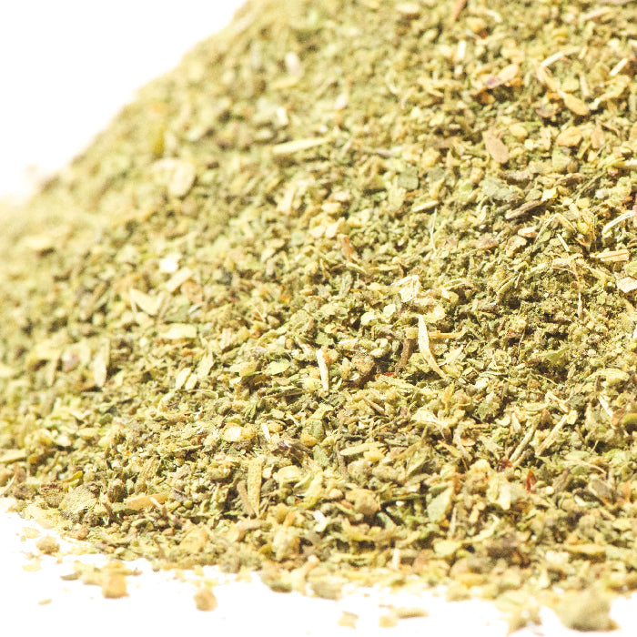 A close-up of Whole Spice Inc. Greek Seasoning—dried, finely ground herbs with small flakes and a powdery texture on a white background. Ideal for pasta salads or as a tasty meat rub.