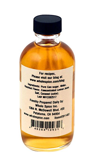 Whole Spice Inc. Hazelnut Syrup comes in a small clear bottle with a black cap, containing light brown hazelnut syrup—perfect for adding rich hazelnut flavor to your coffee or desserts. Ingredients and company details are on the label.
