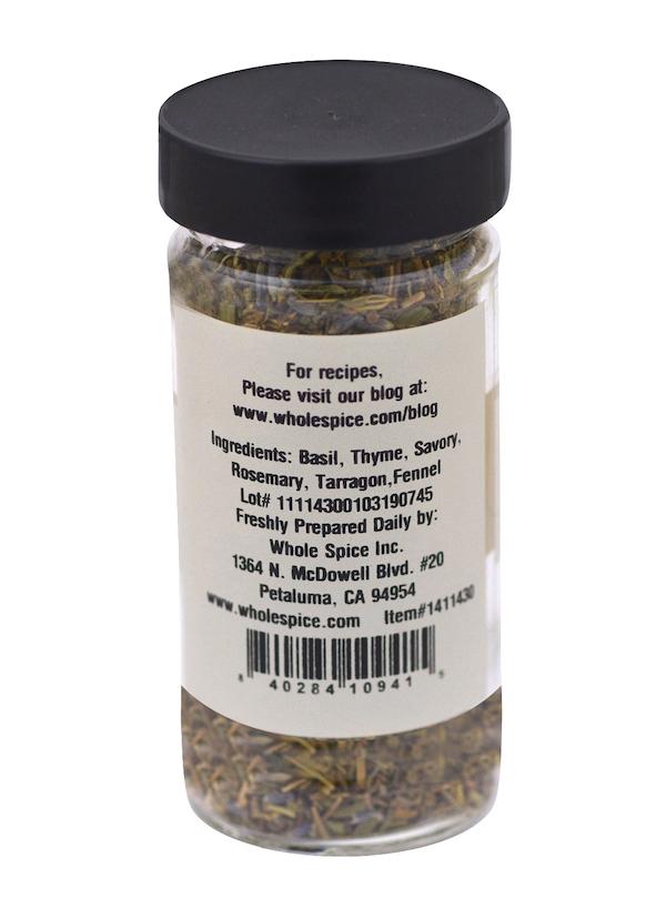 A clear spice jar with a black lid from Whole Spice Inc. holds Herbes de Provence Whole, featuring a white label with ingredients—basil, thyme, savory, rosemary, tarragon, and fennel—plus company contact info. This classic French blend is salt-free.