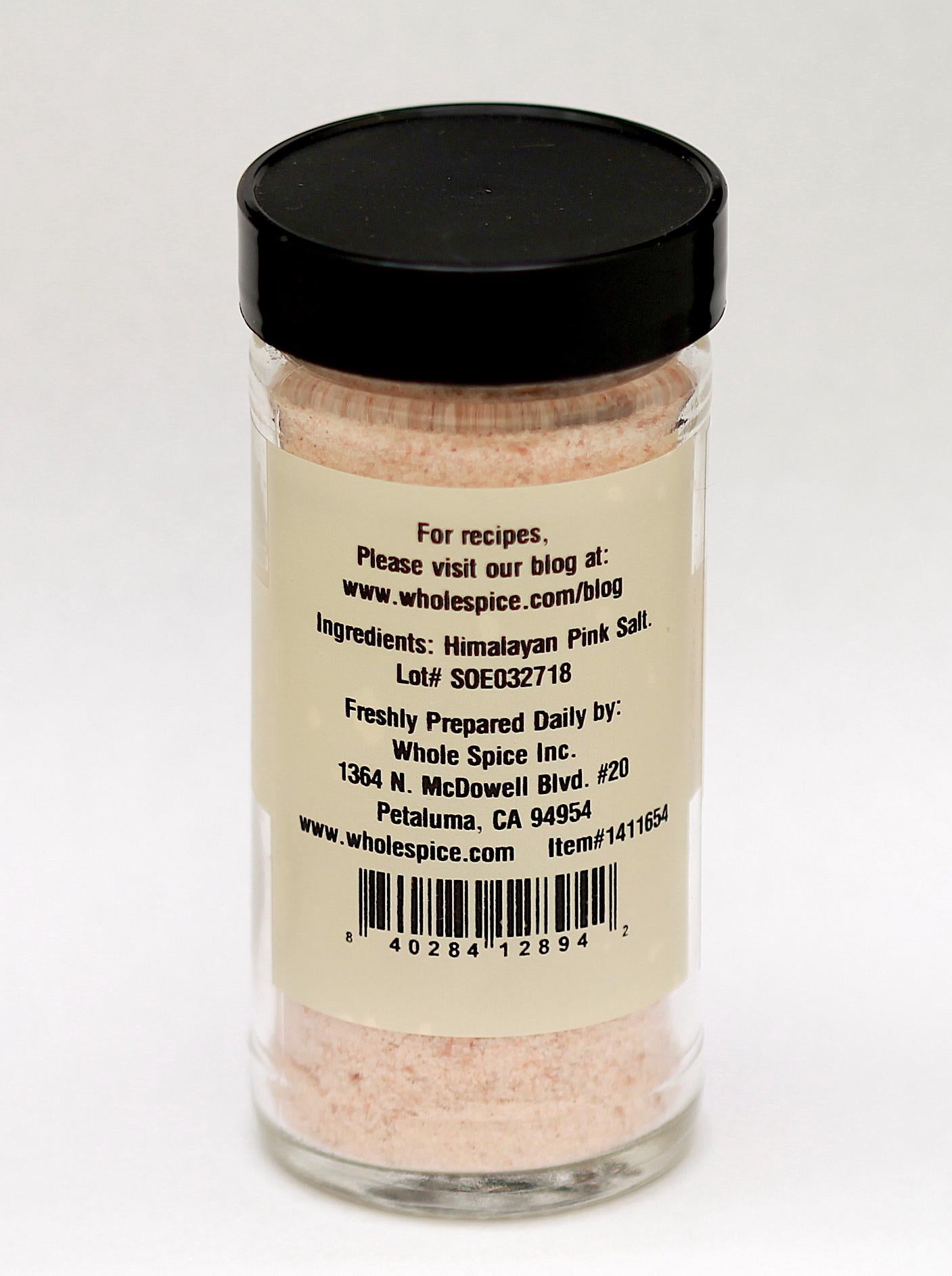 A clear glass jar with a black lid holds Whole Spice Inc. Himalayan Pink Salt Powder (0.0-0.2mm), known for its trace minerals. The back label lists pure salt, contact info, and a barcode.