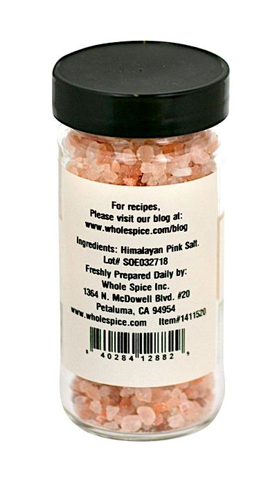 A clear glass jar with a black lid contains Himalayan Pink Salt Coarse (3-5mm) from Whole Spice Inc. The white back label lists ingredients, brand info, and the website for recipes. Rich in trace minerals, the salt crystals are naturally pink.