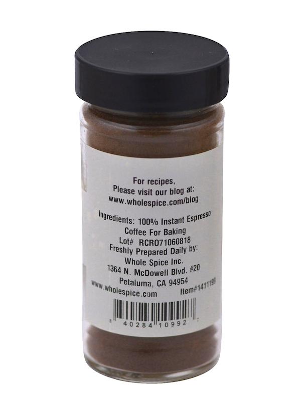 A small clear jar with a black lid holds dark brown Instant Espresso powder by Whole Spice Inc. The label lists 100% instant espresso and includes company info plus a website for coffee drinks and recipes.