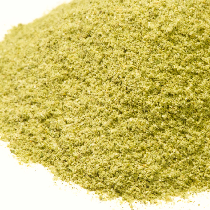 A close-up of Whole Spice Inc.'s Jalapeño Lime Seasoning, a fine, light green powder with a slightly coarse texture, is spread on a white surface.