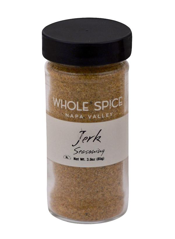 A clear spice jar with a black lid, labeled Whole Spice Inc. Jerk Seasoning, holds 3 oz (85 g) of aromatic Jamaican spice rub in a rich brown blend.