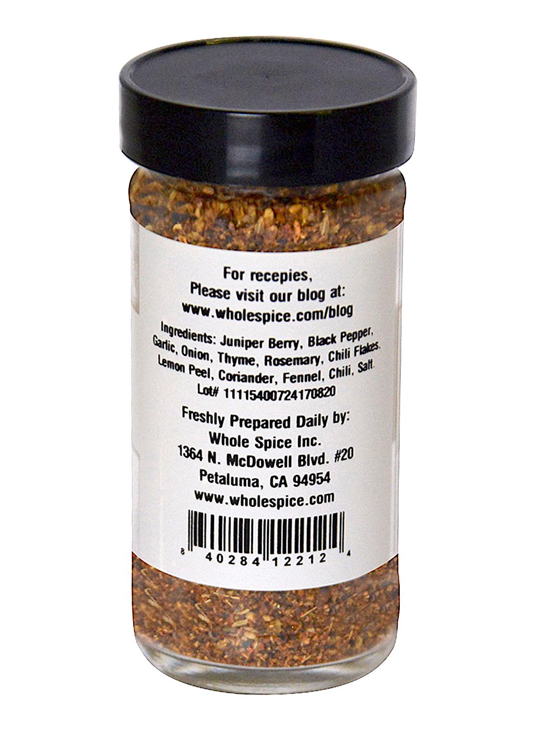 A clear spice jar with a black lid features a label for Juniper Berry Spice Rub by Whole Spice Inc., showing ingredients, contact info, barcode, website, and game meat seasoning details.