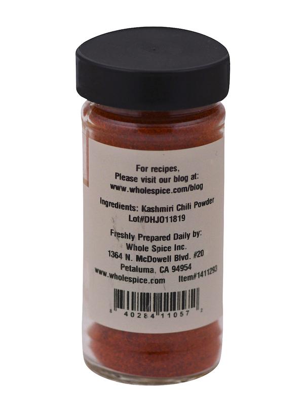 A clear jar with a black lid holds vibrant Kashmiri Chili Powder by Whole Spice Inc. The label features essential spice info, the manufacturer’s address, website, lot number, and recipe ideas for red pepper dishes.