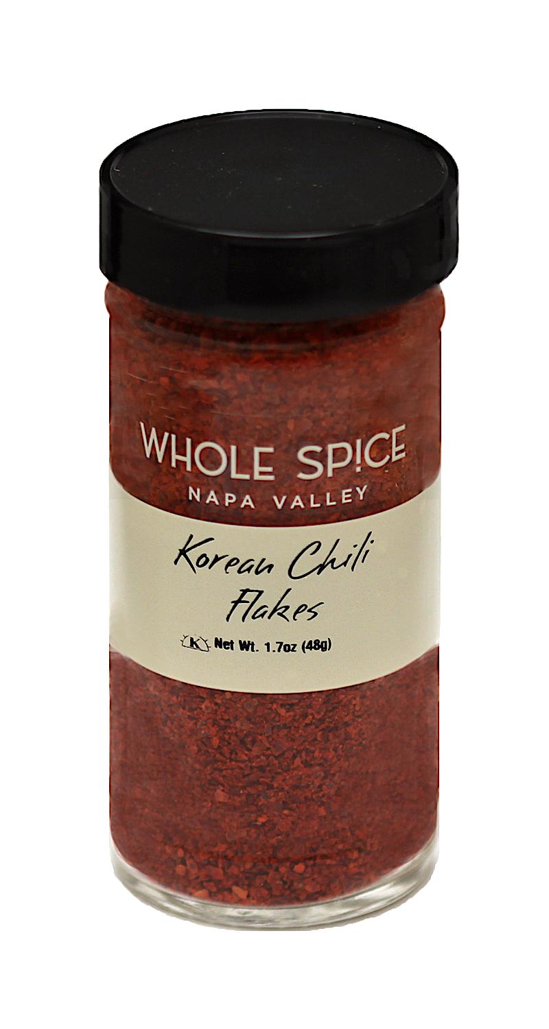 A clear glass jar with a black lid holds red Korean Chili Flakes by Whole Spice Inc., prized for their smoky flavor and mild heat. The label reads: Korean Chili Flakes, Whole Spice Inc., Net Wt. 1.7oz (48g).