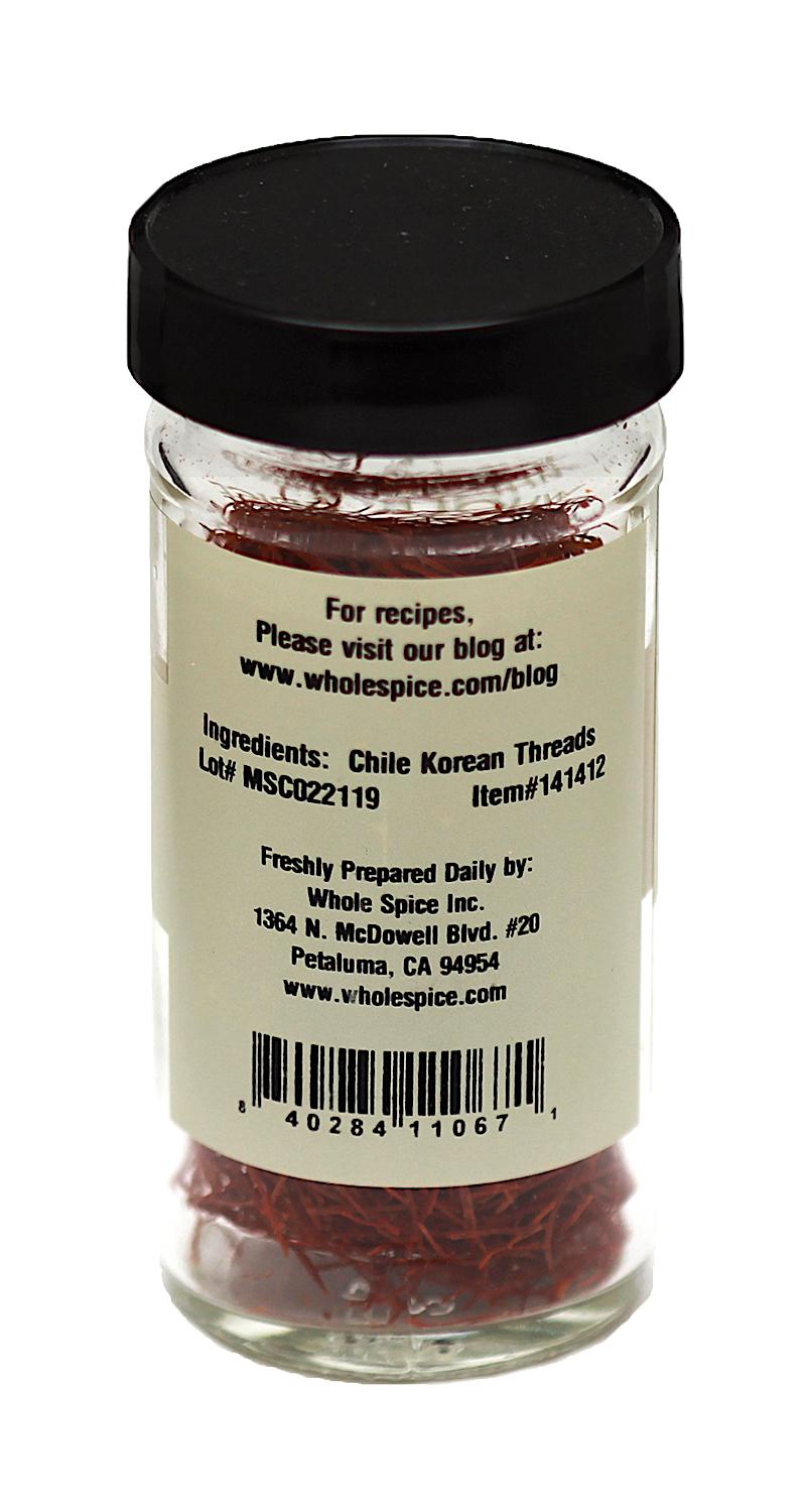 A clear spice jar with a black lid holds Korean Chili Threads. The label lists the ingredient as Chile Korean Threads and features contact and product info from Whole Spice Inc., Petaluma, CA.