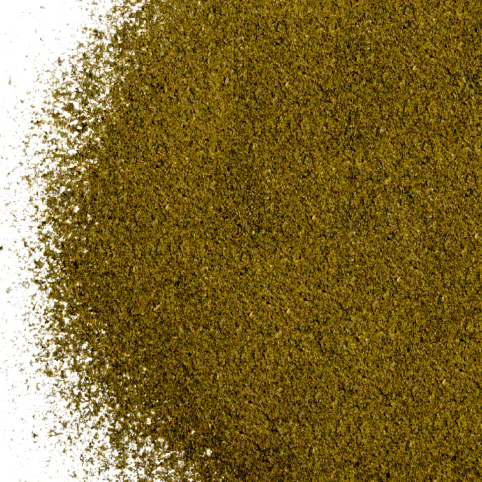 A close-up of finely ground Lapsang Souchong Tea Powder by Whole Spice Inc. shows its greenish-brown color and smoky aroma, with the powder spread across a white background and scattered at the edges.