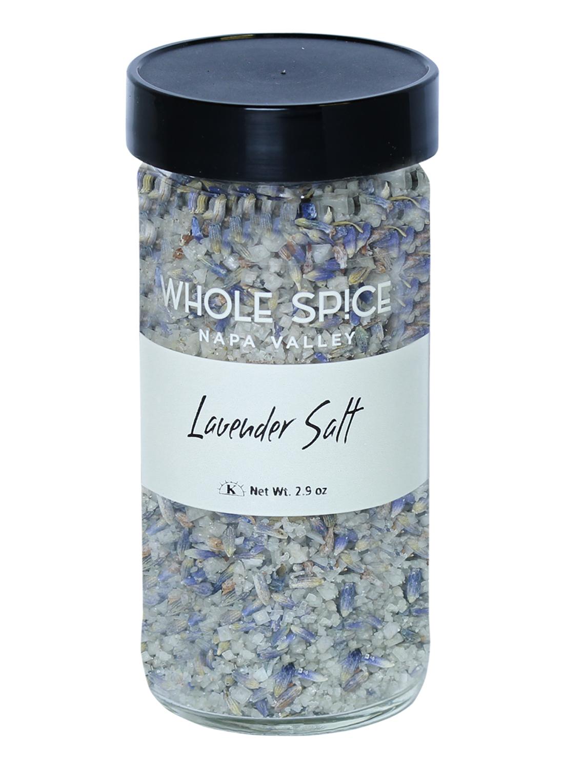 A clear glass jar with a black lid contains Whole Spice Inc. Lavender Salt, a blend of coarse French sea salt and dried lavender, Net Wt. 2.9 oz, shown on a white background.
