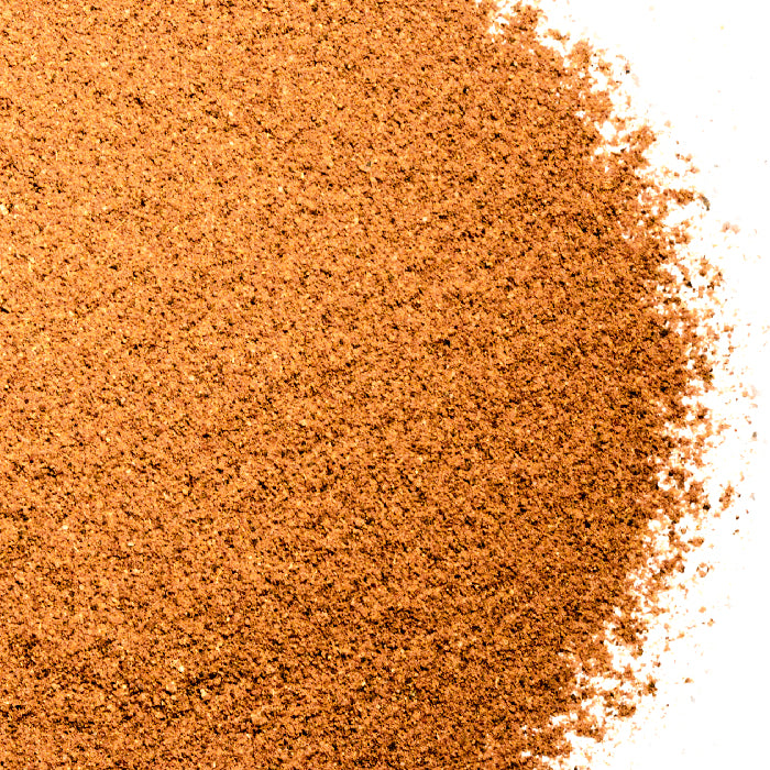 A close-up of fine, light brown Lebanese Seven Spice by Whole Spice Inc. is scattered on a white background, the textured powder dense on the left and gradually thinning to the right.